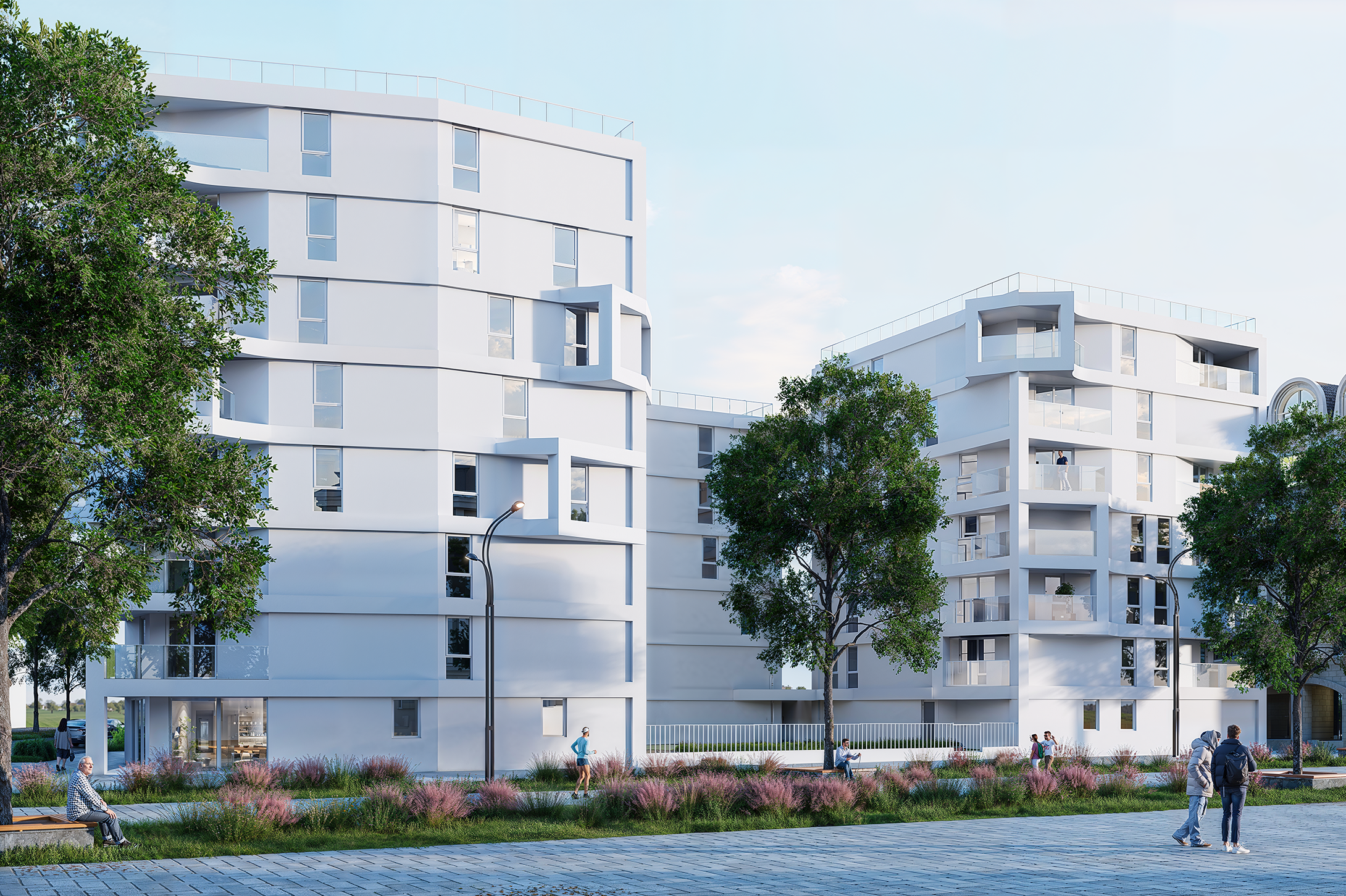 Des immeubles d'appartements blancs modernes aux motifs géométriques, entourés d'arbres et de verdure paysagère. Au premier plan, des passants se promènent et s'assoient sur des bancs le long d'une allée pavée.